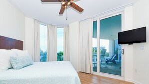 Een slaapkamer met een groot bed, een plafondventilator, een schuifdeur naar een balkon en een flatscreen televisie aan de muur.