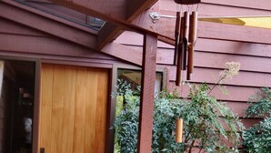 Eine Holzterrasse mit einer Schiebetür, die zu einem Raum führt, umgeben von üppigem Grün und einer gefliesten Terrasse.