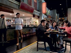 A restaurant with a counter where a server is attending to customers. There are tables with diners, and a sign above the counter indicates the restaurant's name. - Resorts World Awana (Genting Highlands)