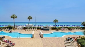 A pool area with lounge chairs and a beach in the background.
