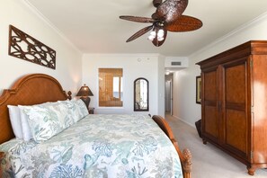 Quarto com cama, cabeceira de madeira, ventilador de teto, guarda-roupa e um detalhe decorativo na parede.