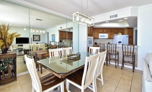 A modern kitchen with a dining area, featuring a glass-top table, wooden chairs, and a central island with a microwave and oven. - Beachfront 3BR condo w/ stunning Gulf views in Destin! 🌺☀ (Destin)