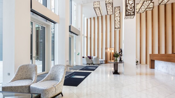 Een ruime lobby met een modern design, met twee armstoelen met een patroon, een receptiebalie en een decoratieve lamp.