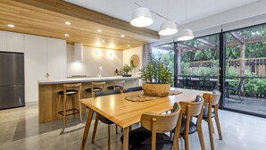Uma cozinha moderna com armários de madeira, geladeira de aço inoxidável e área de refeições com mesa e cadeiras de madeira.