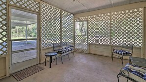 A covered patio area with lattice screens, a bench, a table, and a hanging light fixture. - Pet-Friendly Brooksville Cottage w/ Fire Pit! (Brooksville)
