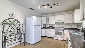 A modern kitchen with white cabinets, a refrigerator, a stove, and a coffee station. - Pet-Friendly Brooksville Cottage w/ Fire Pit! (Brooksville)
