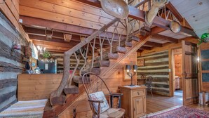 A rustic wooden interior with a wooden staircase, a rocking chair, and a patterned rug.