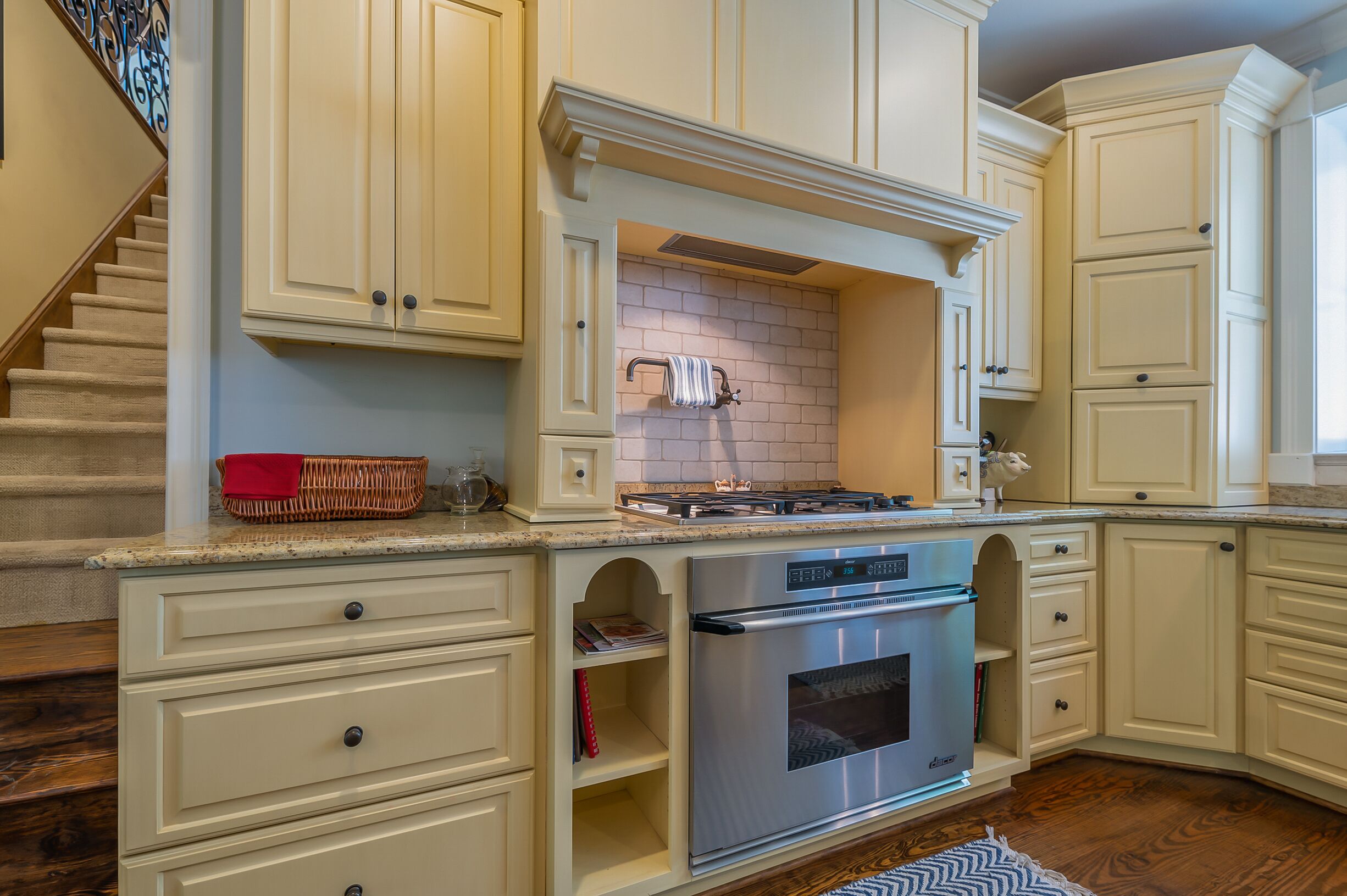 A kitchen with white cabinets, a stainless steel oven, and a brick backsplash.