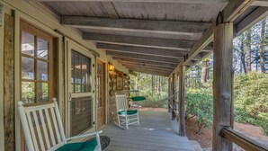 A wooden porch with a rocking chair and a chair with a green cushion.