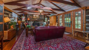 A log cabin interior with a fireplace, wooden beams, a red sofa, and a large window.