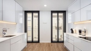A modern kitchen with white cabinetry, a wooden floor, and a view through glass doors to an outdoor balcony. - Stupendo-3br-suite & Terrace- Center- A/conditioning (Lisboa)