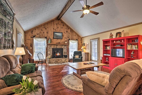 A cozy living room with a fireplace, wooden walls, a ceiling fan, and a red entertainment unit. - ‘Firefly Cove’ - 3 Mi to Parkway & National Park! (Sevierville)