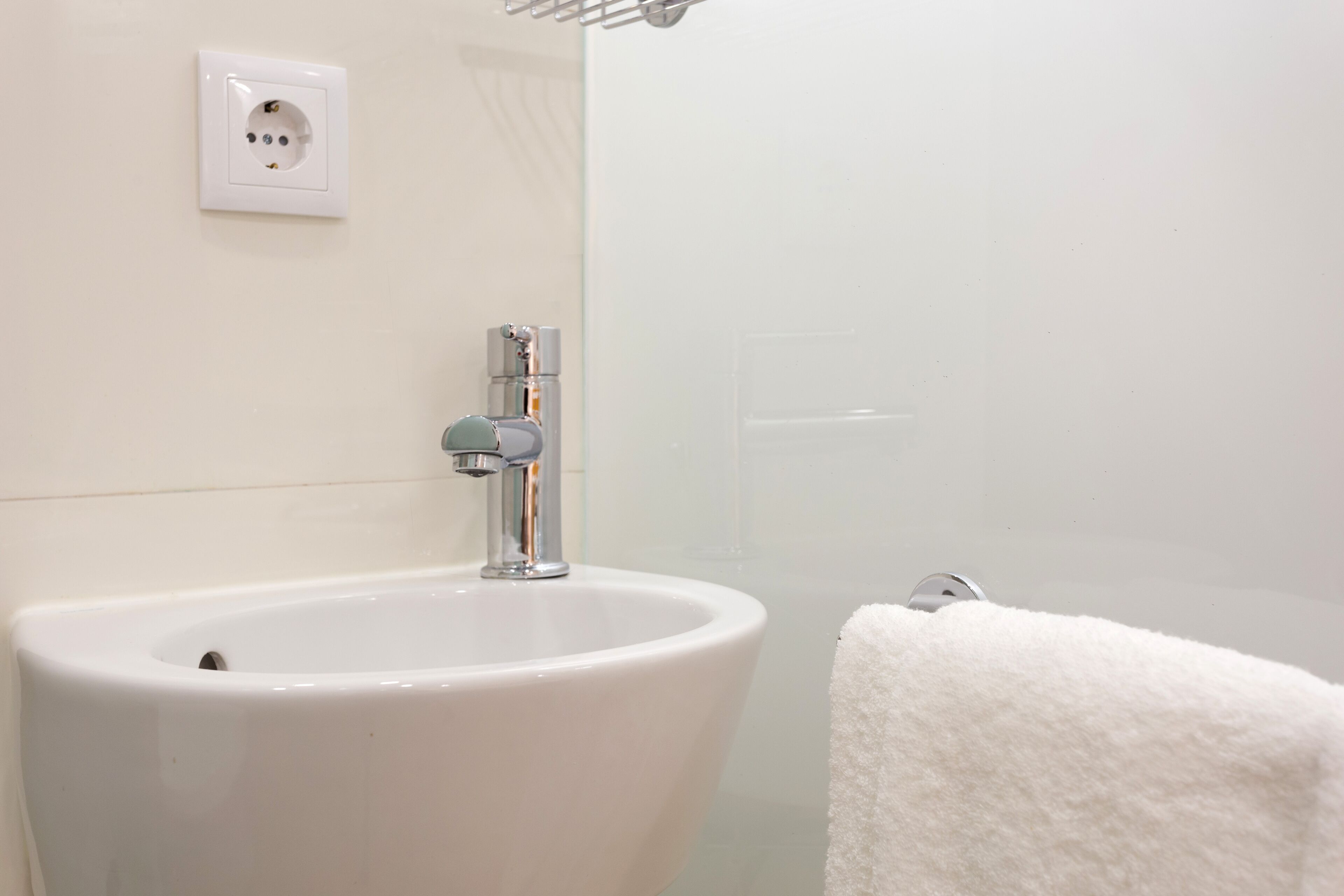 Un baño con un lavabo blanco, un perchero y un enchufe en la pared.