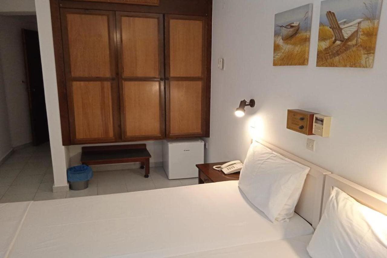 A hotel room with a bed, a small desk, a telephone, a cabinet, and two paintings on the wall.