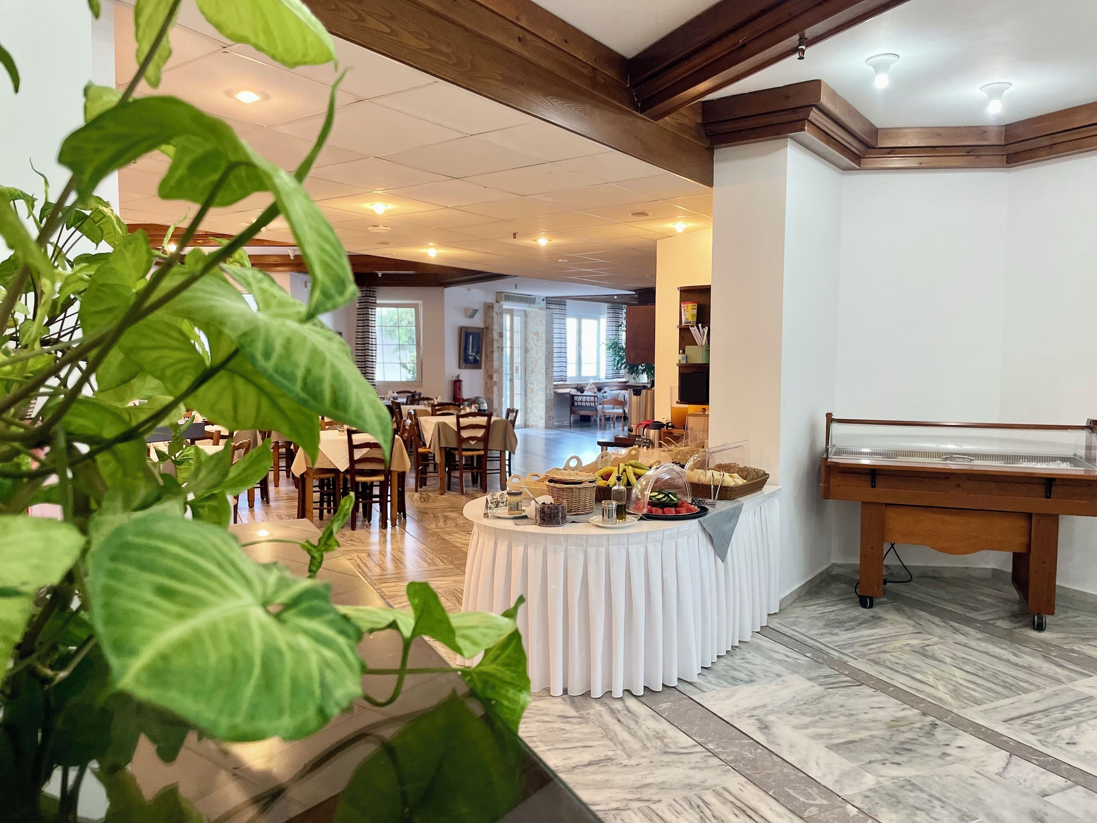 A hotel dining area with a buffet setup, wooden beams on the ceiling, and a view into the dining room.
