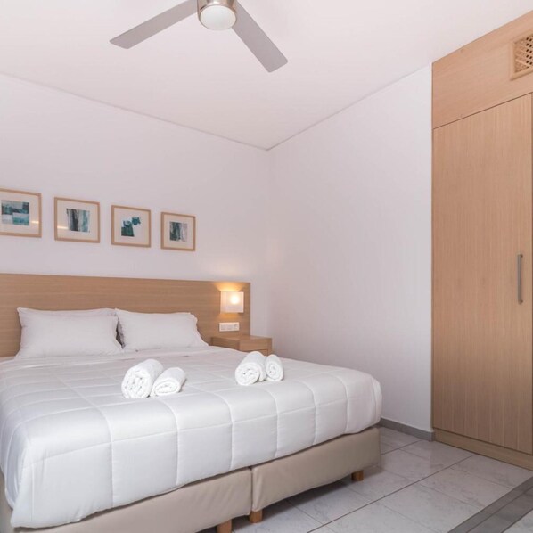 A hotel room with a bed, a ceiling fan, a wardrobe, and framed pictures on the wall. - Pal Beach Hotel (Kantanos-Selino)