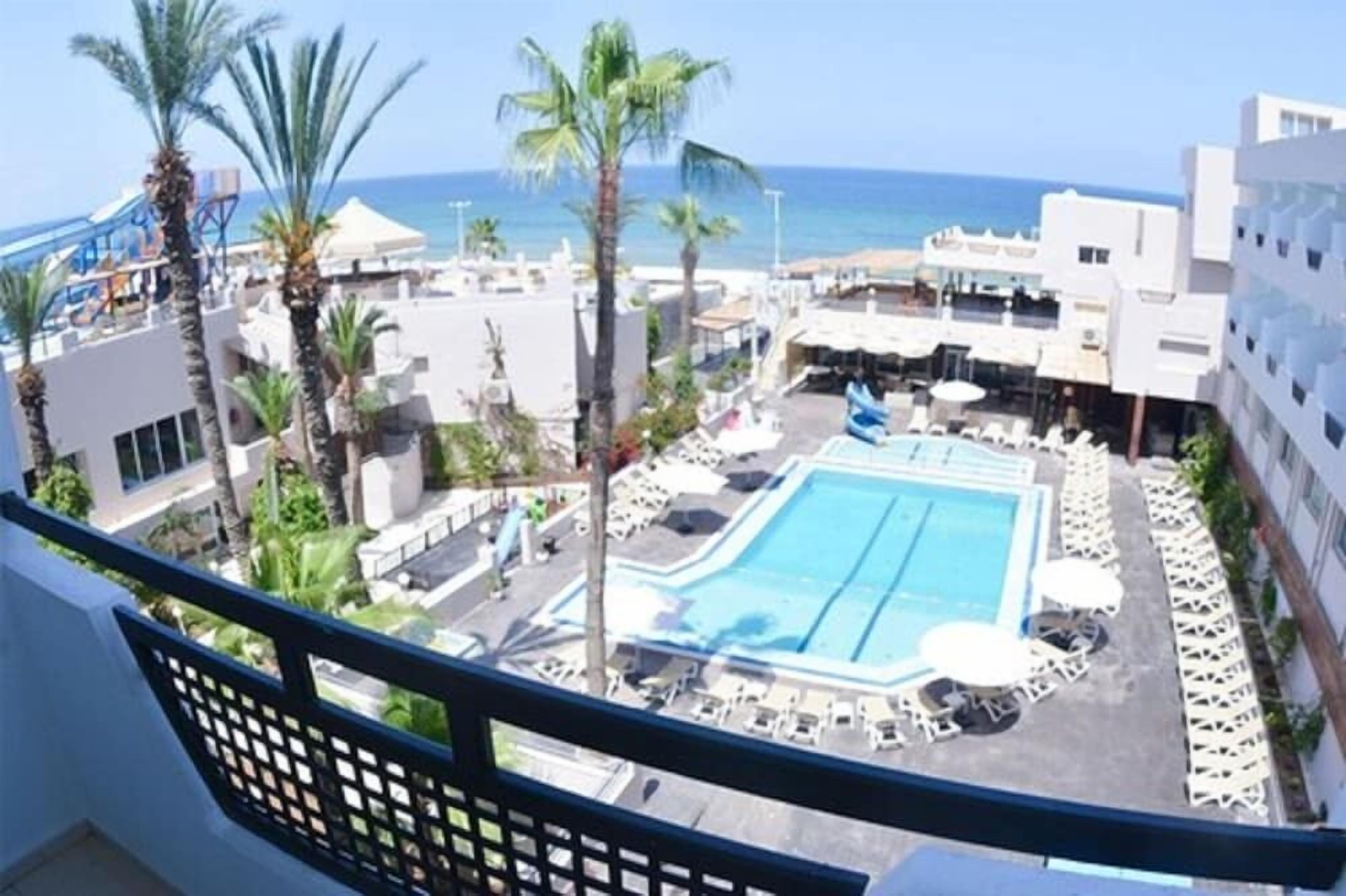 A pool area with lounge chairs, palm trees, and a view of the sea.