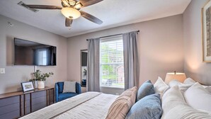 A bedroom with a bed, a ceiling fan, a window with curtains, a bedside table with a lamp, and a TV on the wall. - Modern Condo w/ Deck ~ 7 Mi To Branson Landing! (Branson)