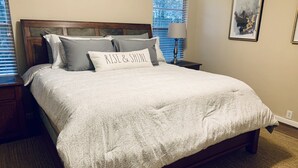 A neatly made bed with a white comforter and pillows, a wooden headboard, a bedside table with a lamp, and a framed picture on the wall. - Inviting/Cozy Home in Medical Center - Beautiful home to stay!!  (Houston)