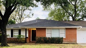 A single-story house with a brick facade, a dark roof, and a garage. - Inviting/Cozy Home in Medical Center - Beautiful home to stay!!  (Houston)