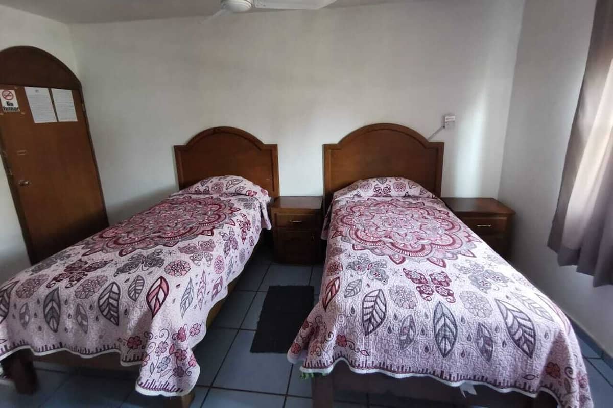 Una habitación con dos camas individuales, cabeceros de madera, un ventilador de techo y suelo de baldosas.