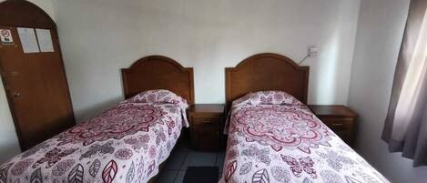 A room with two single beds, wooden headboards, a ceiling fan, and a tiled floor.