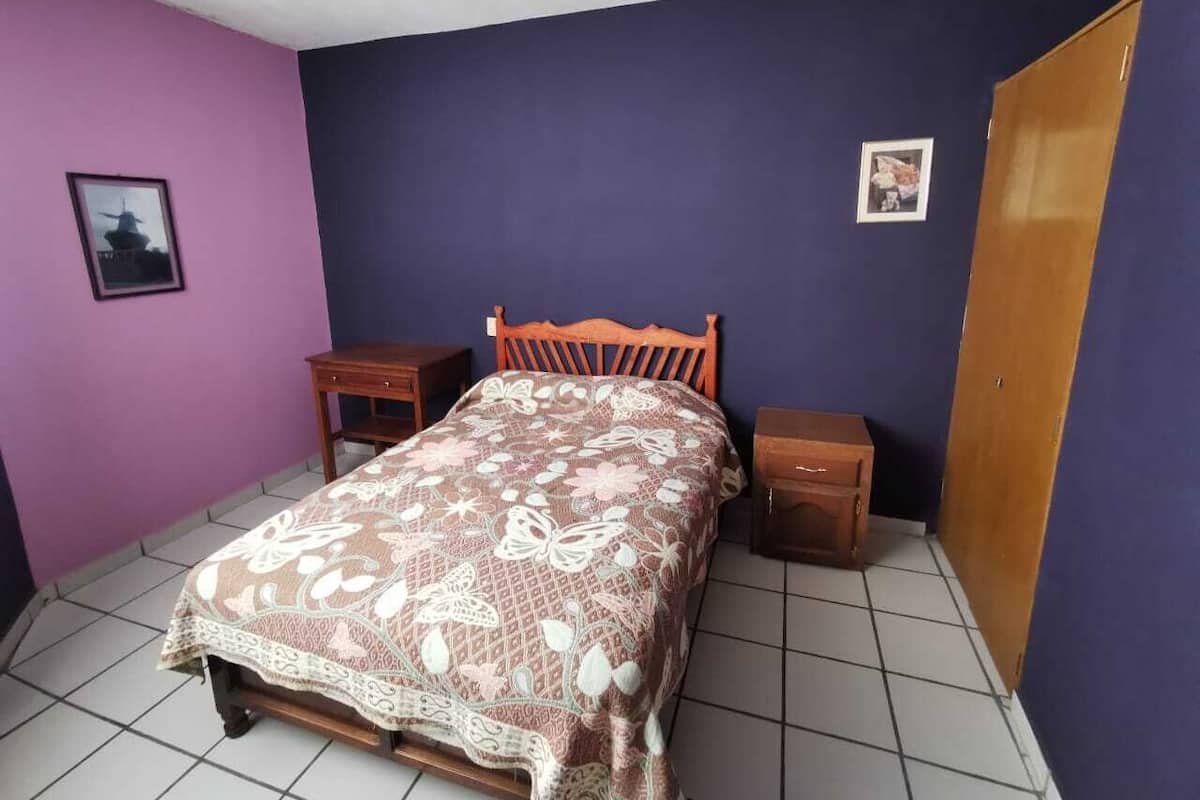 Un dormitorio con cama, mesita de noche, armario de madera y una pequeña mesa.