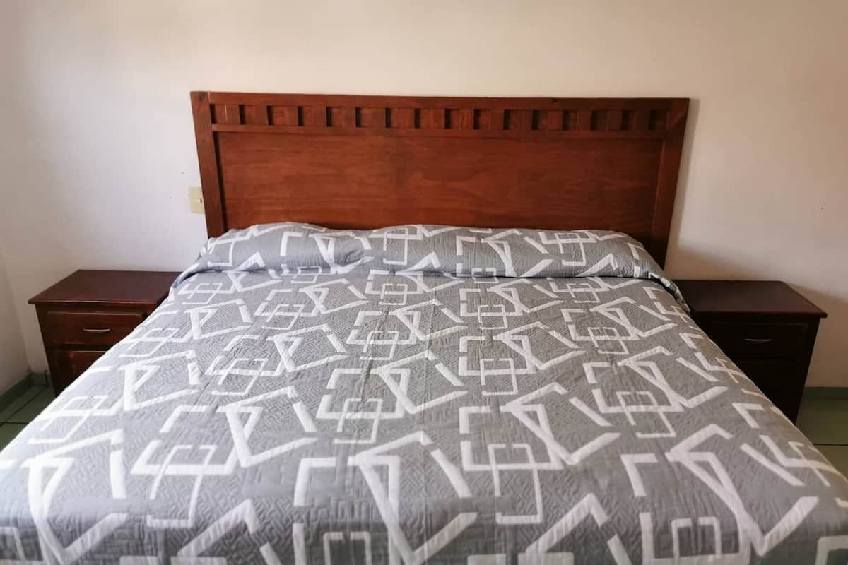 Una cama con colcha de estampado geométrico, cabecera de madera y dos mesitas de noche con cajones.