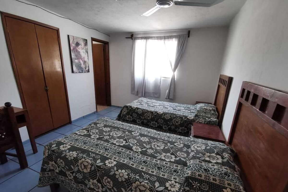 Un dormitorio con dos camas, un armario de madera, una silla y un ventilador de techo.
