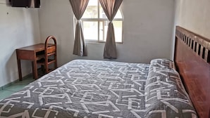 A bedroom with a bed, a desk, and a TV mounted on the wall.