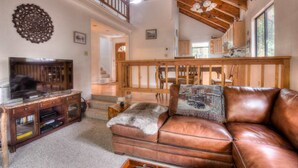 A spacious living room with a leather sofa, wooden entertainment unit, and a staircase leading to an upper level.