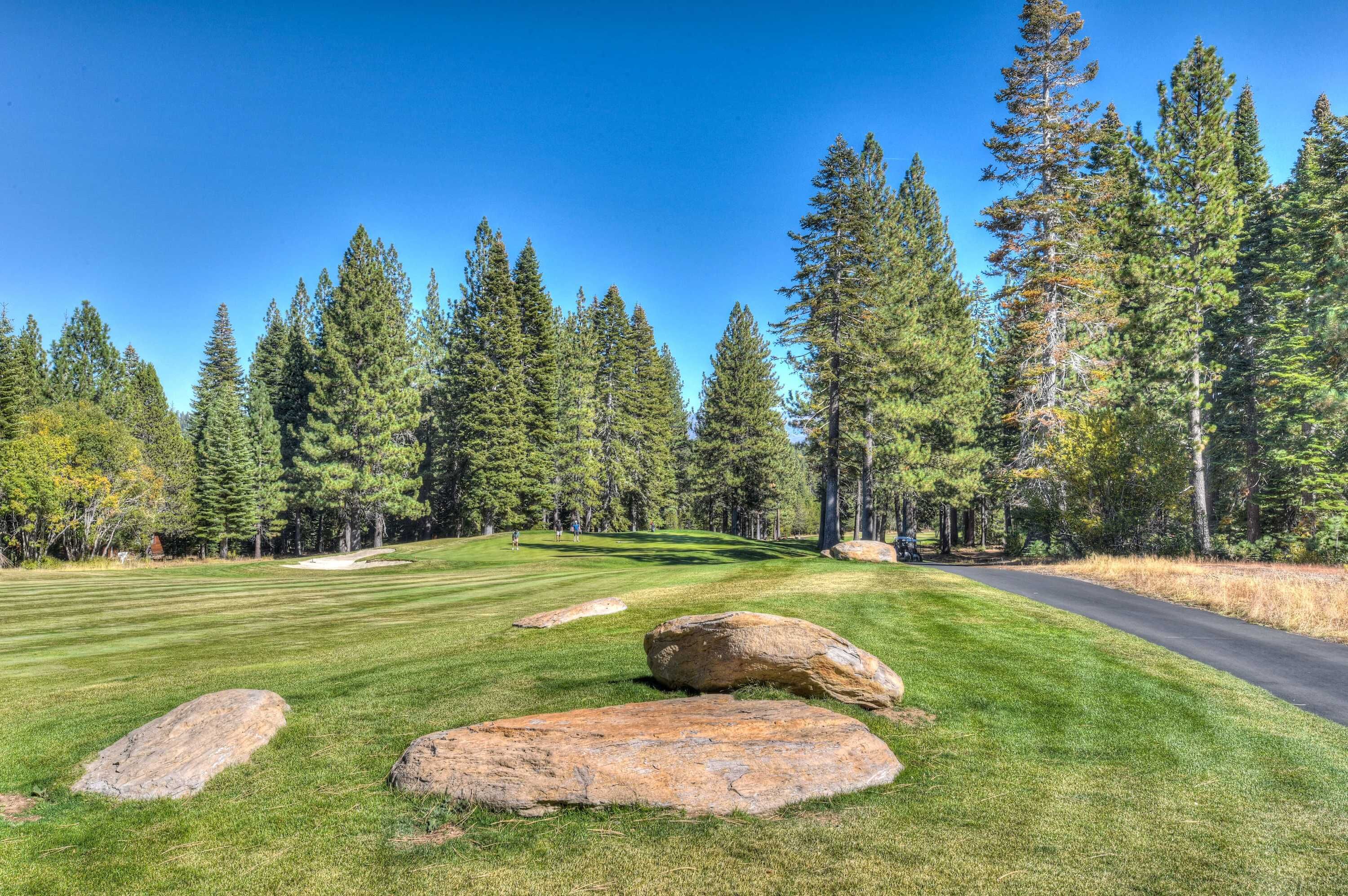 A golf course with a clear sky, green grass, and large rocks.