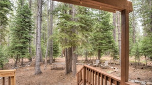 A wooden deck with a picnic table and chairs, surrounded by a forest.