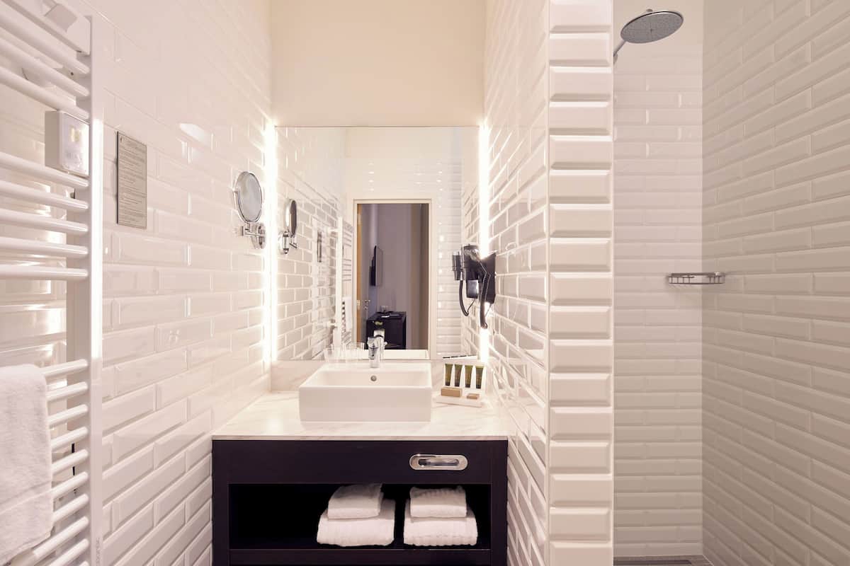 A modern bathroom with white subway tiles, a white sink, a mirror, a towel rack, and a shower.