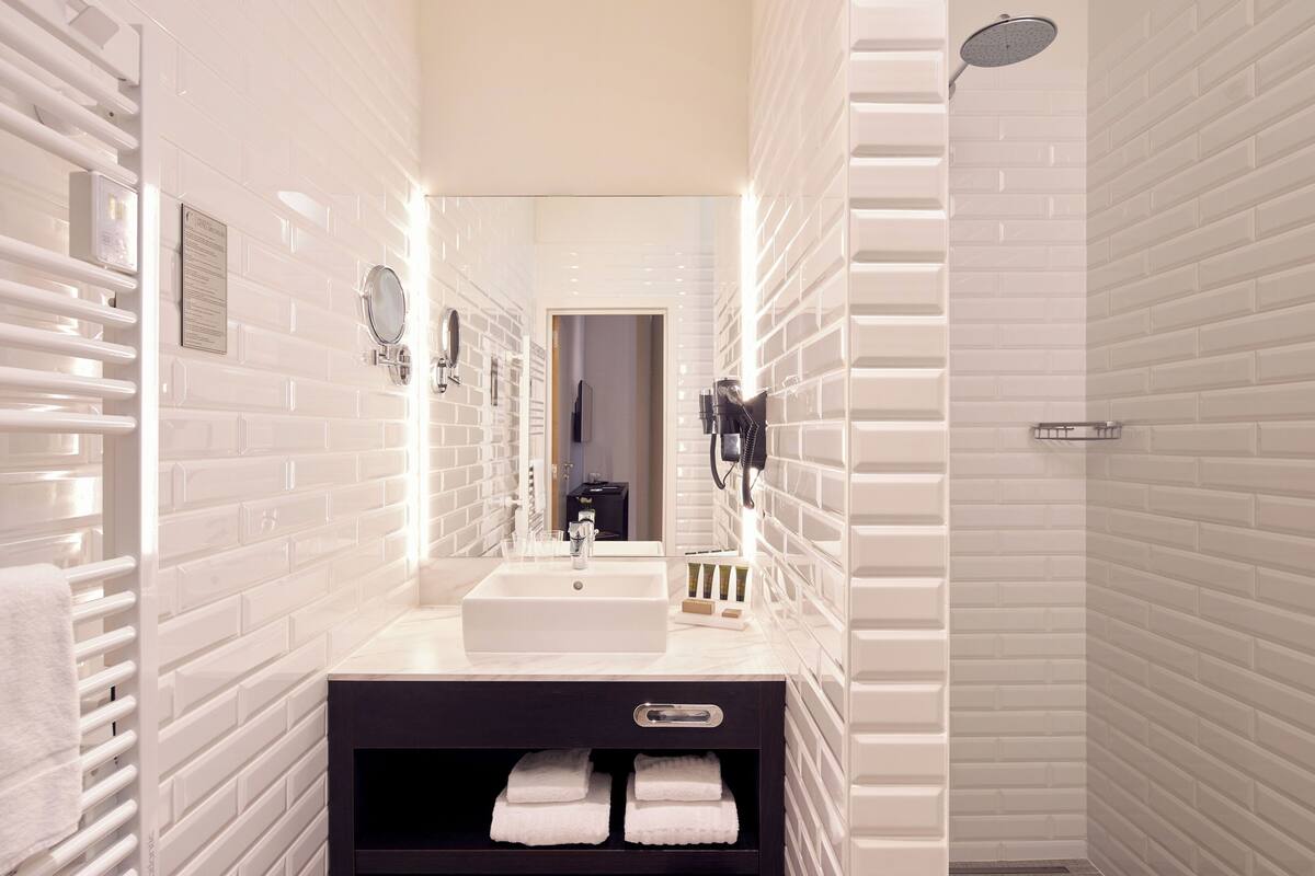 Un baño moderno con azulejos blancos tipo metro, un lavabo blanco, un espejo, un perchero para toallas y una ducha.