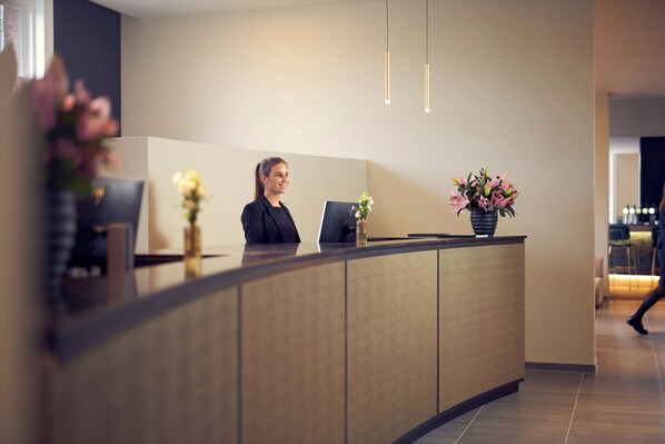 Una recepción con una recepcionista, una computadora y dos arreglos florales.