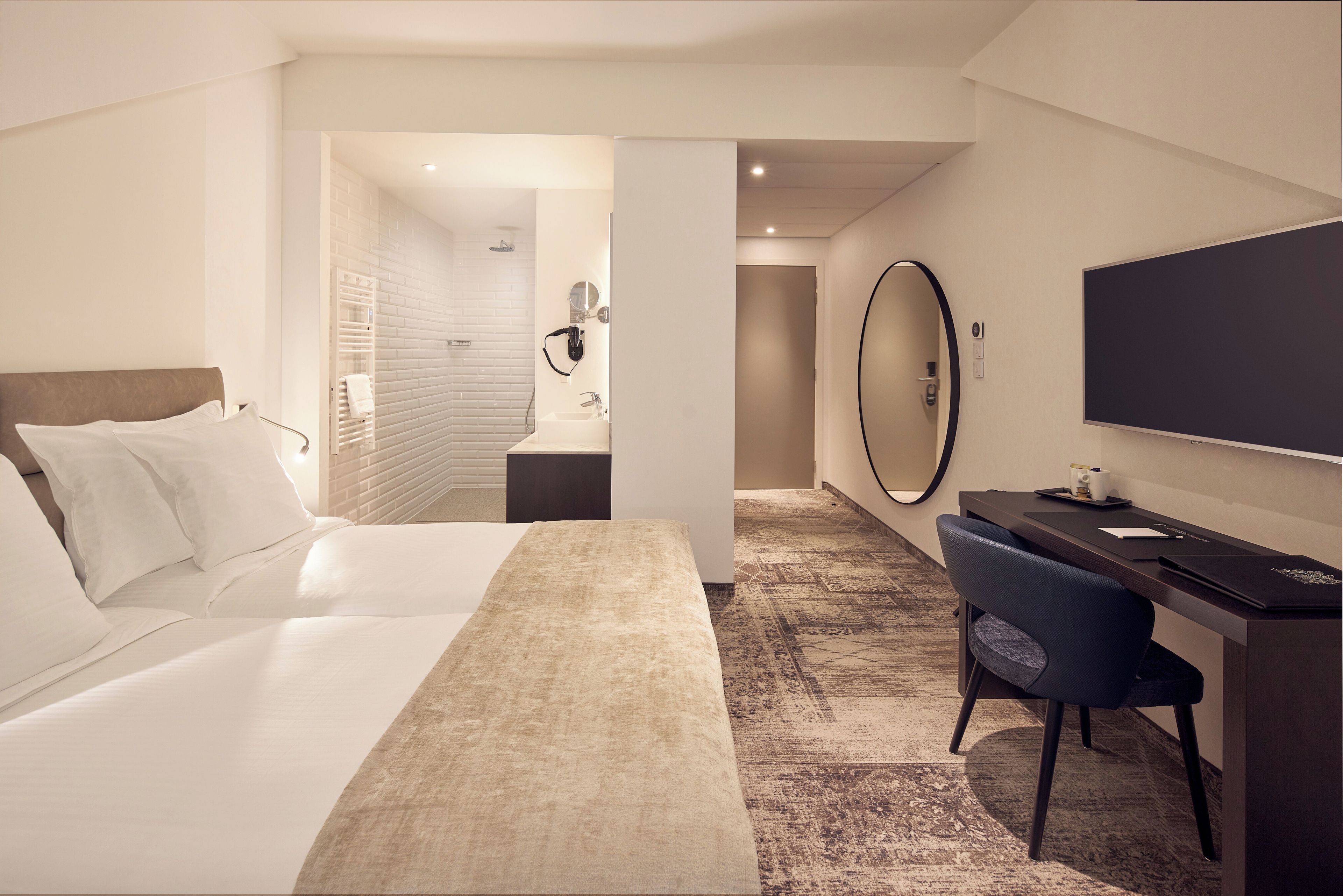 Een hotelkamer met een bed, een bureau, een stoel, een grote spiegel en een televisie.