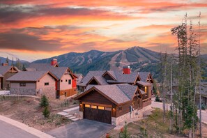 Un ensemble de maisons de style rustique, construites en rondins de bois, avec une vue sur les montagnes, comprenant plusieurs garages et une allée bien entretenue.