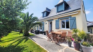 A two-story house with a patio area featuring a table and chairs, surrounded by potted plants and a well-maintained lawn. - Phil'blue by Interhome (Saint Philibert)