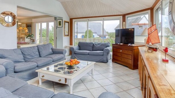 A spacious living room with a high ceiling, large windows, and a television. - Phil'blue by Interhome (Saint Philibert)