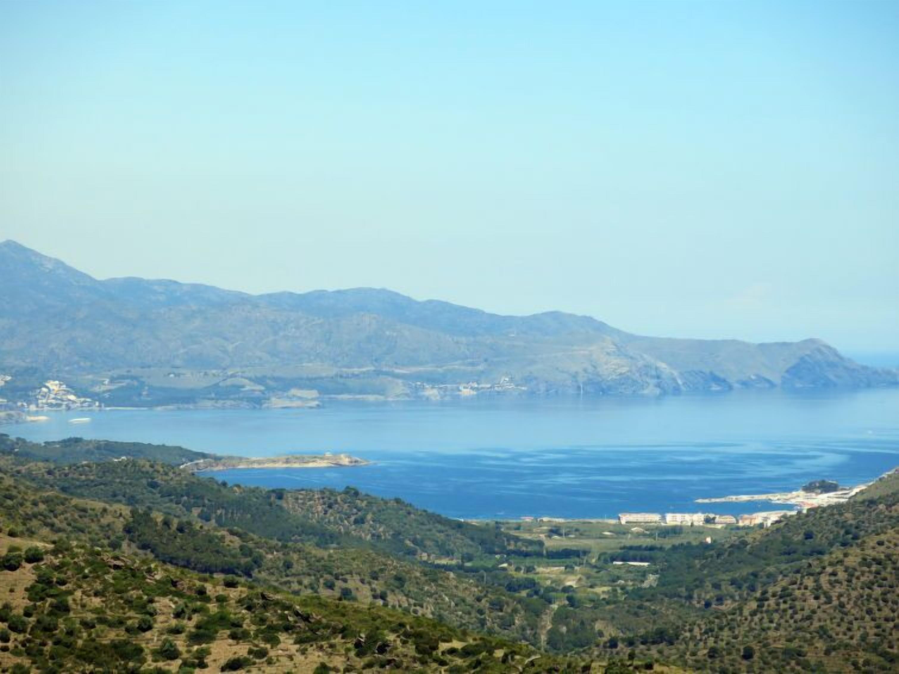 A coastal landscape with mountains, a body of water, and a building complex.