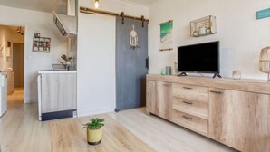 Moderni keittiö, jossa on keskeinen saareke, ruokapöytä, jonka päällä on ruukkukasvi, ja televisio puukehikossa.