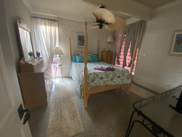 A bedroom with a four-poster bed, a nightstand, a dresser, a mirror, and a ceiling fan.