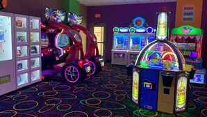 An arcade with neon-lit machines, a prize hub, and a colorful floor pattern.