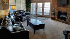 A living room with a leather sofa, a coffee table, a fireplace, and a stone wall.