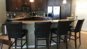 A modern kitchen with dark wood cabinets, a central island with bar stools, stainless steel appliances, and a tiled backsplash.