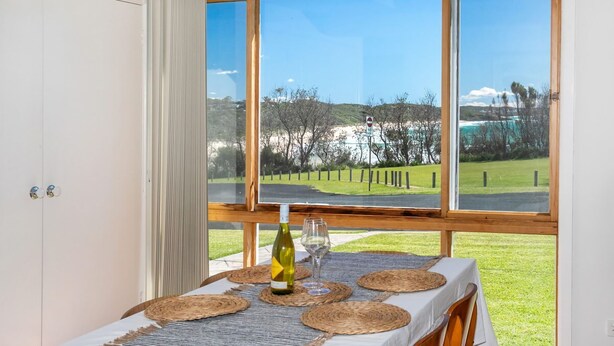 Un coin repas avec une table dressée pour deux, une bouteille de vin et un verre, le tout placé sur une table offrant une vue sur un paysage verdoyant et des arbres, grâce à de grandes fenêtres.
