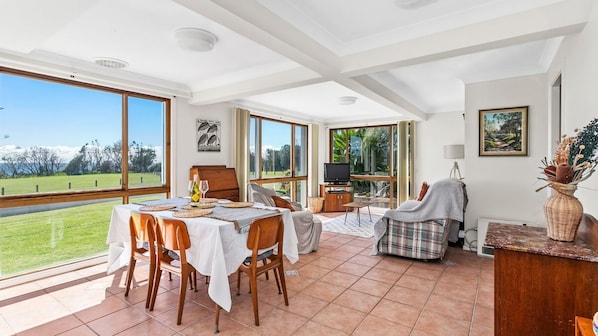 A spacious dining area with a view of a grassy field and mountains, a television, and a cozy seating area with a blanket. - FREE NIGHT. Pay for 2 stay for 3 (Dolphin Point)