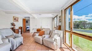 Ein geräumiges Wohnzimmer mit großem Fenster, Essbereich und Blick ins Freie.
