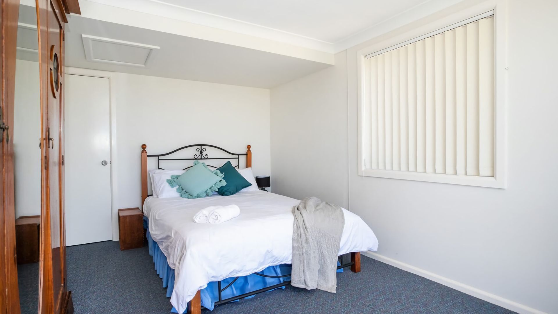 Un dormitorio con una cama, una mesita de noche, una ventana con persianas y una puerta.